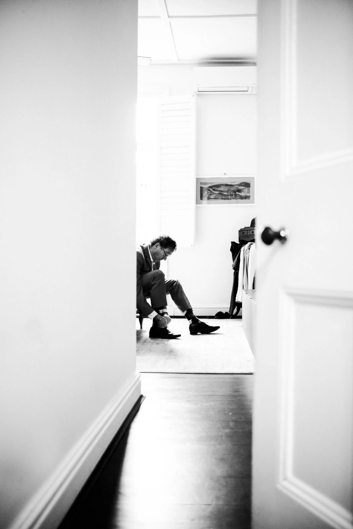 Black-and-white photograph down a hallway of Andrew getting ready
